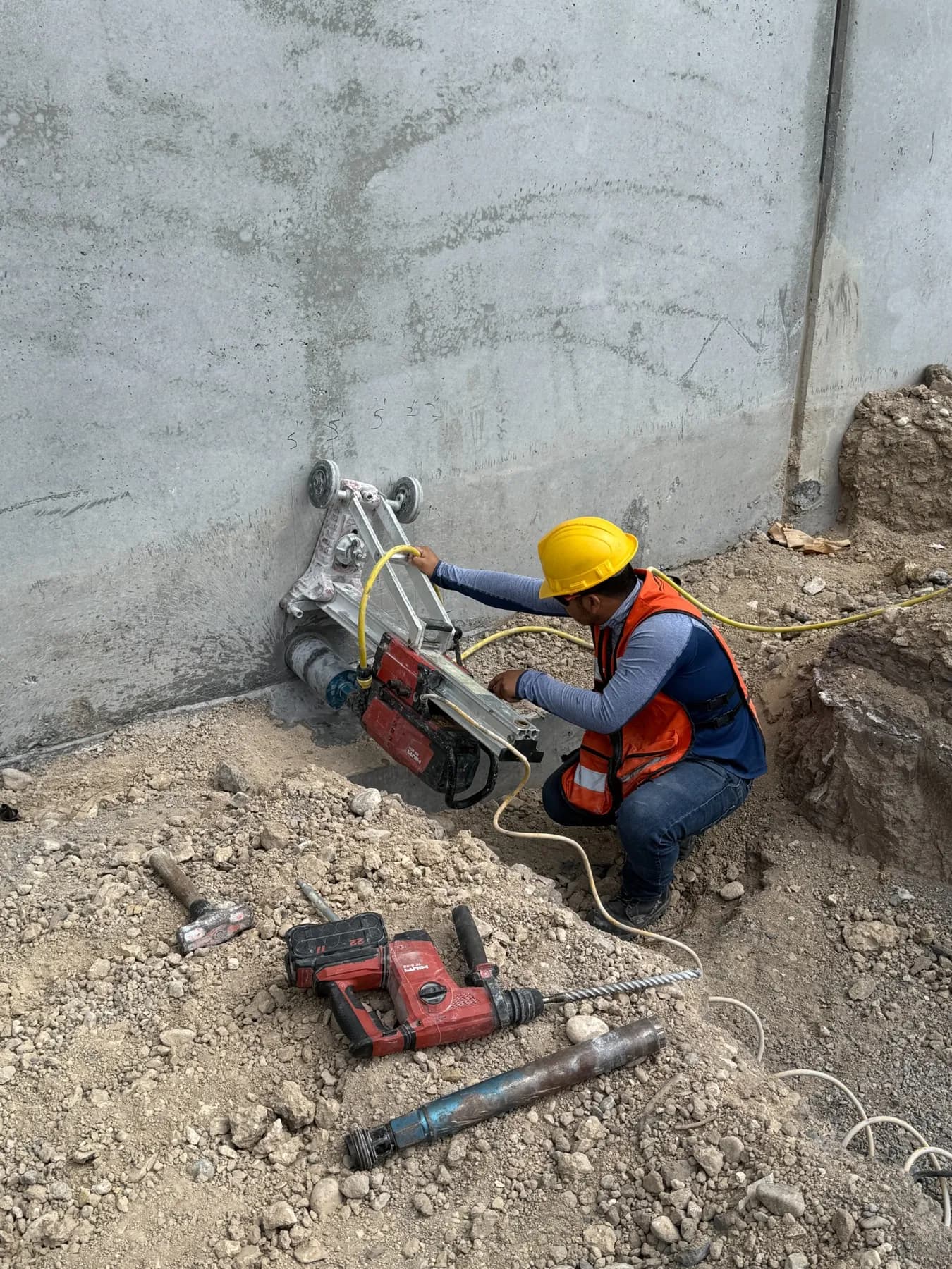 Operario con casco y chaleco de seguridad realizando una perforación en un muro de concreto durante una obra